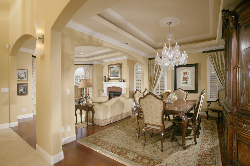 Traditional dining room in San Diego with yellow walls, a standard fireplace and a wood fireplace surround.