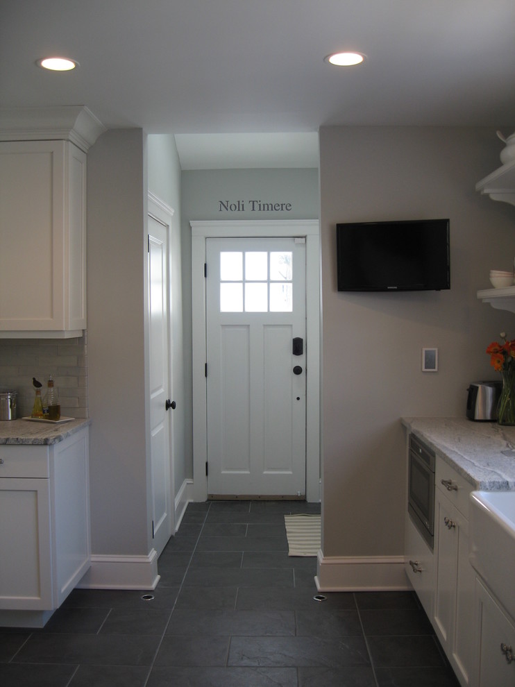 Eat-in kitchen - transitional slate floor eat-in kitchen idea in New York with a farmhouse sink, recessed-panel cabinets, white cabinets and paneled appliances