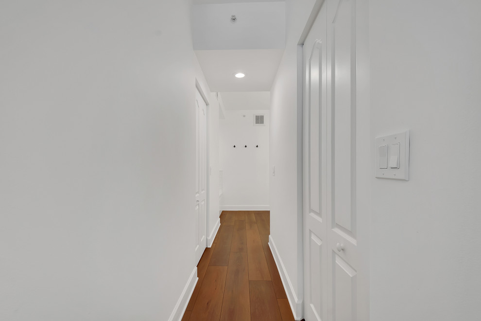 Modern inredning av en mellanstor hall, med vita väggar, vinylgolv och brunt golv
