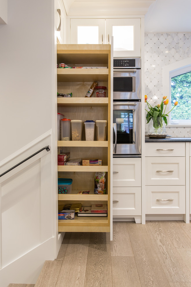 Example of a large transitional l-shaped medium tone wood floor and beige floor eat-in kitchen design in Vancouver with an undermount sink, shaker cabinets, white cabinets, granite countertops, gray backsplash, marble backsplash, stainless steel appliances, an island and black countertops