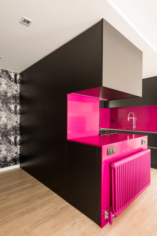 This is an example of a mid-sized modern galley open plan kitchen in Barcelona with a single-bowl sink, flat-panel cabinets, quartz benchtops, pink splashback, stainless steel appliances, medium hardwood floors, a peninsula and brown floor.