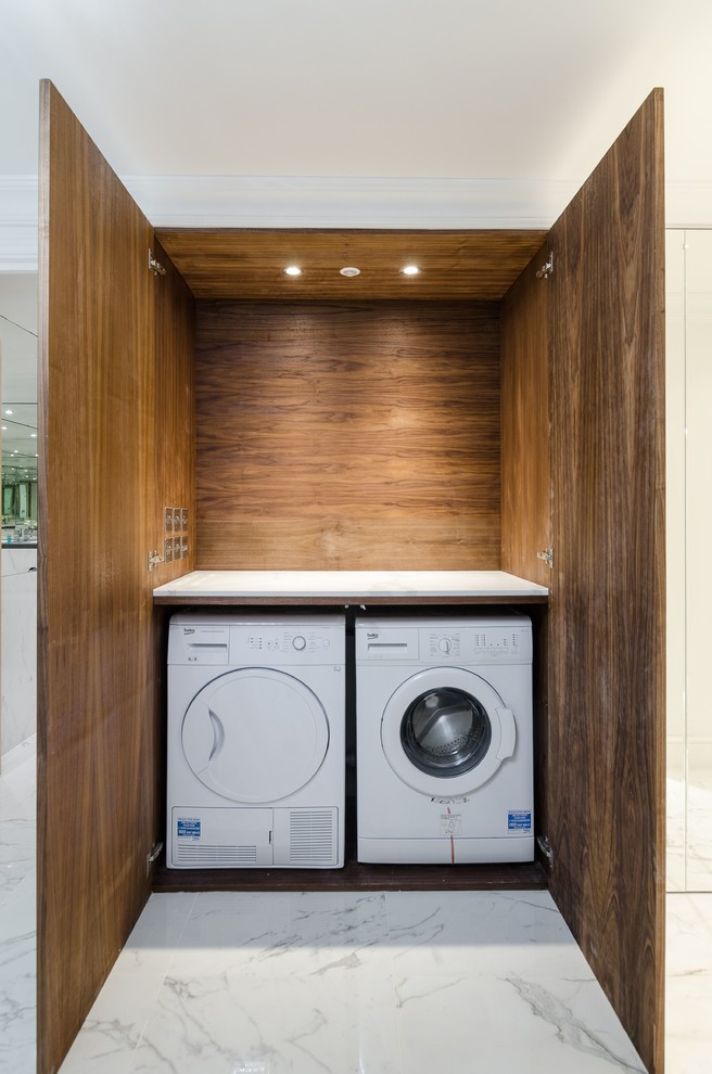 Small modern single-wall laundry cupboard in London with dark wood cabinets, marble benchtops and a side-by-side washer and dryer.