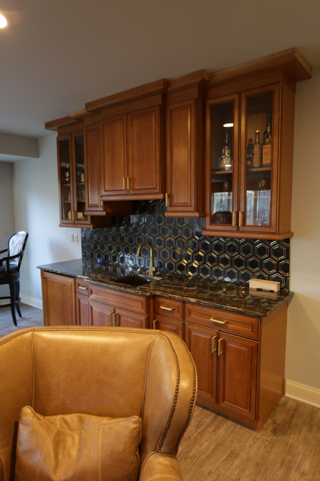 This is an example of a mid-sized traditional single-wall wet bar in Baltimore with an undermount sink, raised-panel cabinets, medium wood cabinets, granite benchtops, black splashback, marble splashback, plywood floors, beige floor and black benchtop.