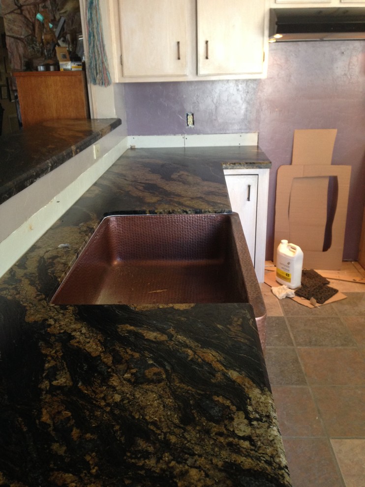 Eat-in kitchen - mid-sized transitional l-shaped limestone floor and brown floor eat-in kitchen idea in Phoenix with a farmhouse sink, recessed-panel cabinets, white cabinets, granite countertops, stainless steel appliances and black countertops
