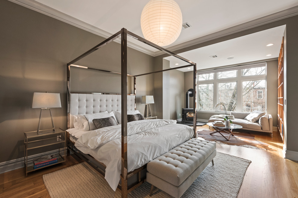 Transitional master bedroom in New York with grey walls, medium hardwood floors, a wood stove and brown floor.