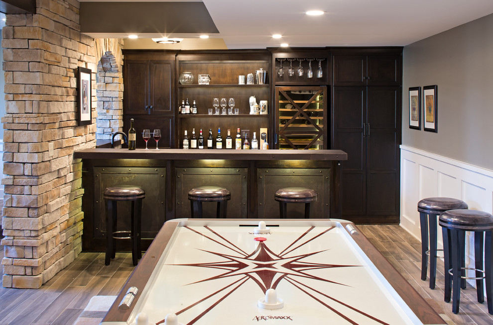 Photo of a mid-sized industrial single-wall seated home bar in Chicago with flat-panel cabinets, dark wood cabinets, stainless steel benchtops, porcelain floors and brown floor.