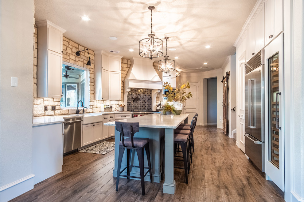 Large galley eat-in kitchen in Houston with a farmhouse sink, shaker cabinets, white cabinets, quartzite benchtops, multi-coloured splashback, stone tile splashback, stainless steel appliances, porcelain floors, with island, brown floor and multi-coloured benchtop.