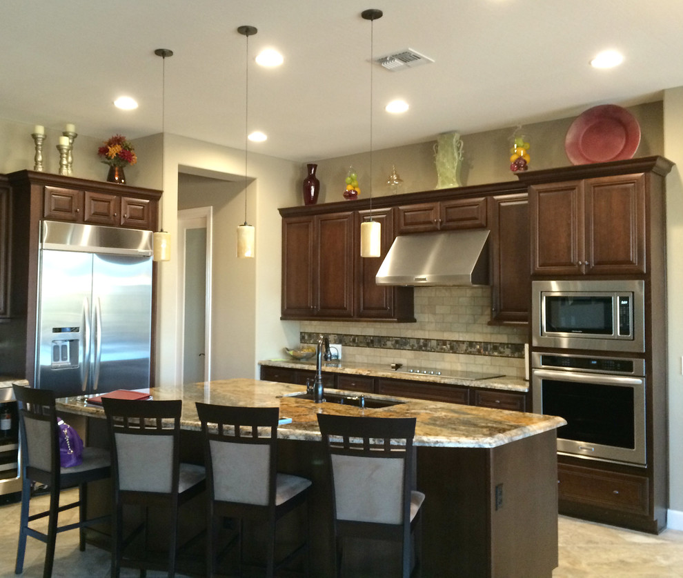 Example of a mid-sized transitional l-shaped ceramic tile and brown floor open concept kitchen design in Phoenix with an undermount sink, raised-panel cabinets, dark wood cabinets, granite countertops, metallic backsplash, mosaic tile backsplash, stainless steel appliances and an island