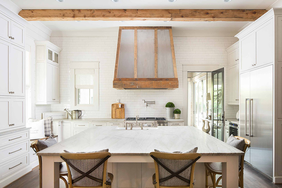 Photo of a country u-shaped kitchen in Atlanta with a farmhouse sink, recessed-panel cabinets, white cabinets, white splashback, stainless steel appliances, medium hardwood floors, with island, brown floor and grey benchtop.