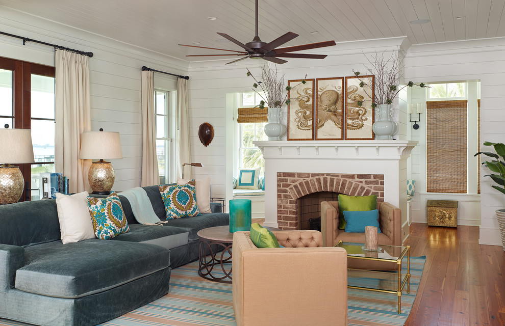 This is an example of a tropical living room in Charleston with white walls, a standard fireplace, a brick fireplace surround and no tv.