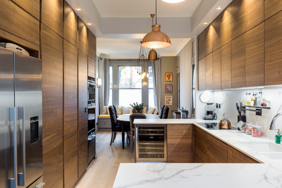 This is an example of a contemporary u-shaped kitchen in London with a double-bowl sink, flat-panel cabinets, medium wood cabinets, marble benchtops, white splashback, stone tile splashback, stainless steel appliances, light hardwood floors and a peninsula.