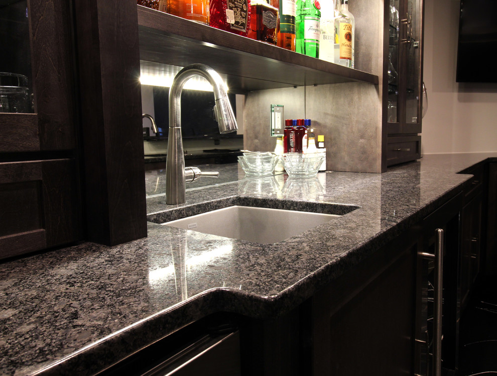 Photo of a mid-sized transitional u-shaped seated home bar in Chicago with an undermount sink, glass-front cabinets, dark wood cabinets, granite benchtops, linoleum floors, black floor and black benchtop.