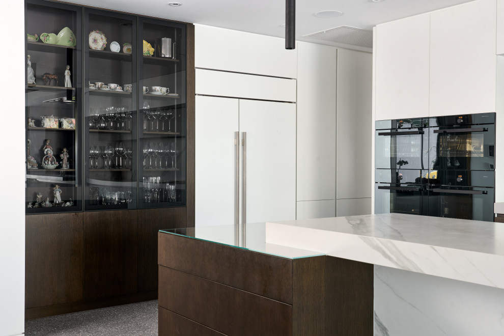 Design ideas for an expansive contemporary l-shaped eat-in kitchen in Perth with an undermount sink, flat-panel cabinets, white cabinets, quartz benchtops, white splashback, porcelain splashback, black appliances, concrete floors, with island, grey floor and white benchtop.