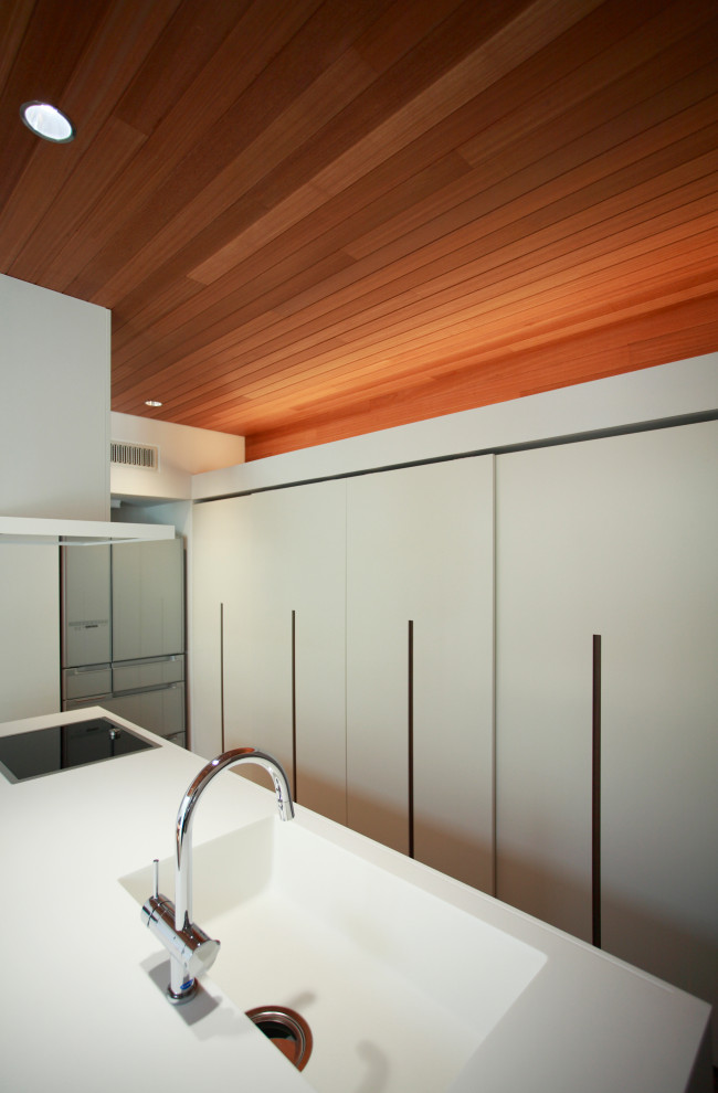 Пример оригинального дизайна: прямая кухня-гостиная в стиле модернизм с монолитной мойкой, плоскими фасадами, столешницей из акрилового камня, островом и белой столешницей