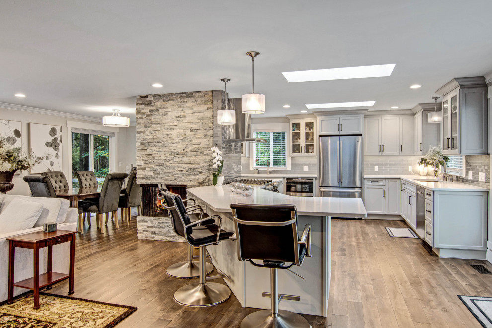 Transitional medium tone wood floor and brown floor open concept kitchen photo in Seattle with an undermount sink, recessed-panel cabinets, gray cabinets, quartz countertops, gray backsplash, subway tile backsplash, stainless steel appliances, a peninsula and white countertops