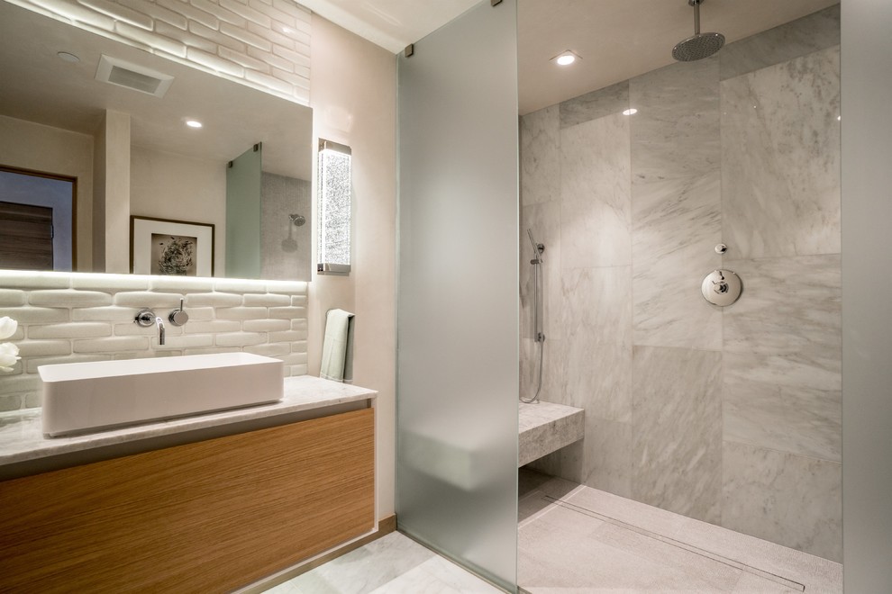This is an example of a large contemporary master bathroom in Other with flat-panel cabinets, light wood cabinets, a curbless shower, a wall-mount toilet, green tile, marble, multi-coloured walls, marble floors, a vessel sink, solid surface benchtops, white floor, an open shower and beige benchtops.