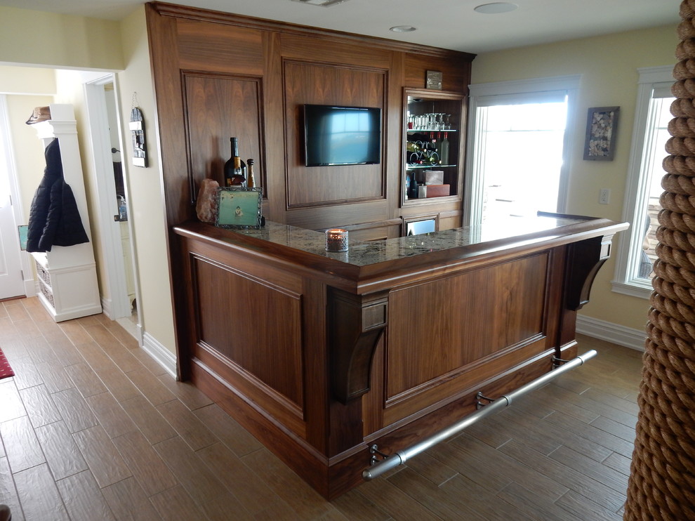 This is an example of a mid-sized traditional l-shaped home bar in Philadelphia with no sink, medium wood cabinets, granite benchtops, medium hardwood floors and brown floor.