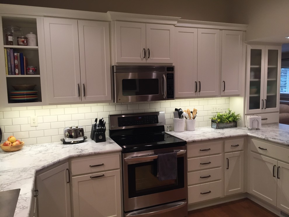 Example of a mid-sized transitional u-shaped medium tone wood floor eat-in kitchen design with an integrated sink, shaker cabinets, white cabinets, laminate countertops, white backsplash, subway tile backsplash, stainless steel appliances and a peninsula