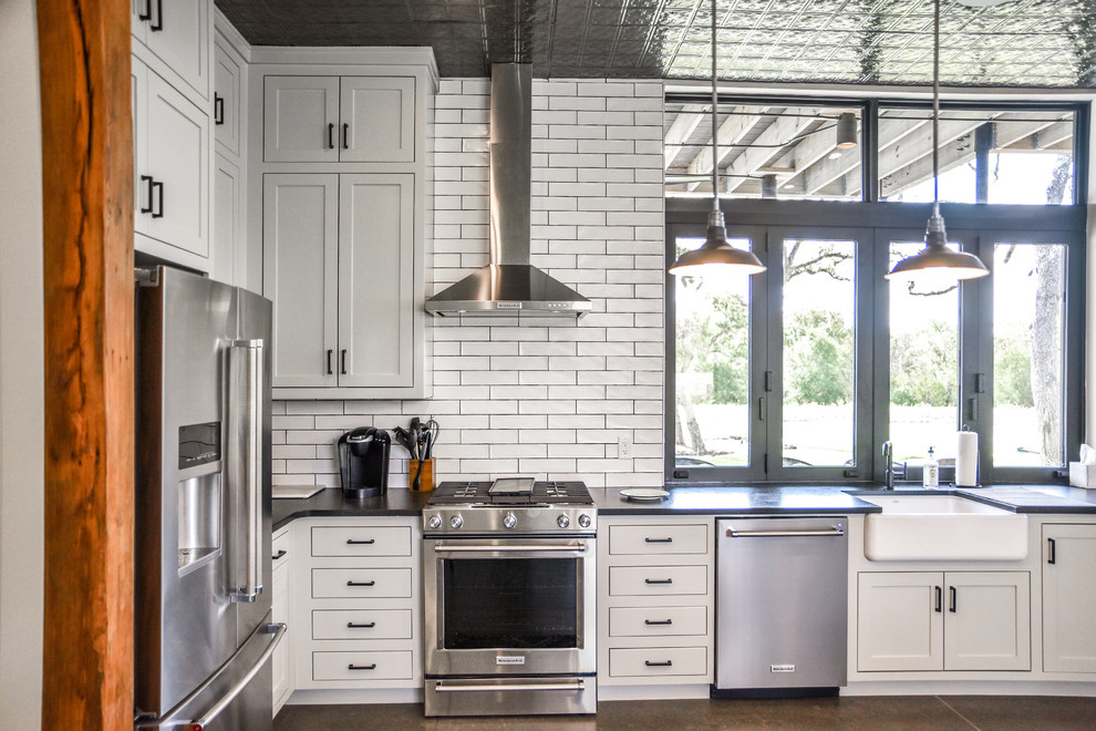 Design ideas for a mid-sized modern u-shaped open plan kitchen in Austin with a farmhouse sink, shaker cabinets, grey cabinets, granite benchtops, white splashback, subway tile splashback, stainless steel appliances, concrete floors, a peninsula, grey floor and black benchtop.