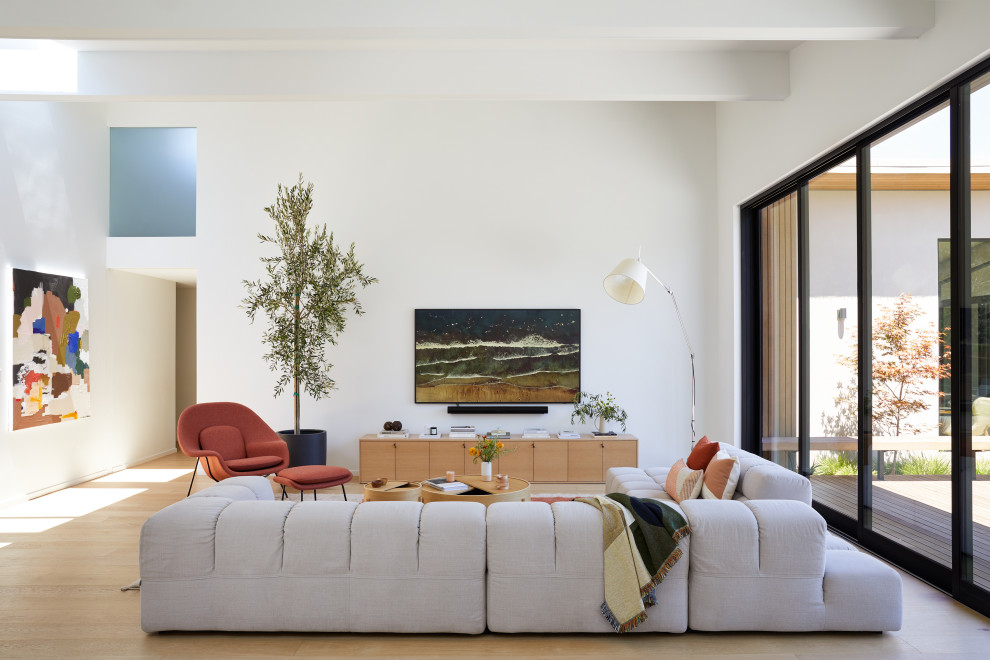 Пример оригинального дизайна: большая открытая гостиная комната в стиле модернизм с домашним баром, белыми стенами, светлым паркетным полом, телевизором на стене, балками на потолке и бежевым полом без камина