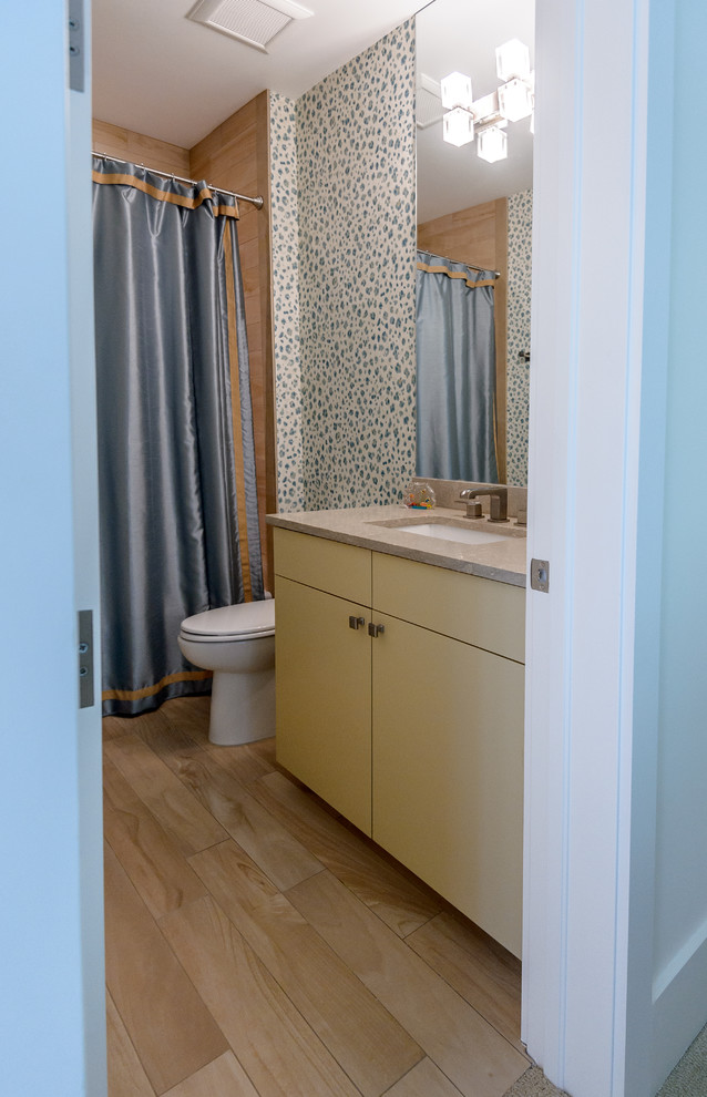 Mid-sized beach style 3/4 bathroom in Charleston with flat-panel cabinets, a one-piece toilet, beige tile, porcelain tile, porcelain floors, an undermount sink, an alcove shower, quartzite benchtops, beige floor, yellow cabinets, an alcove tub, multi-coloured walls and a shower curtain.