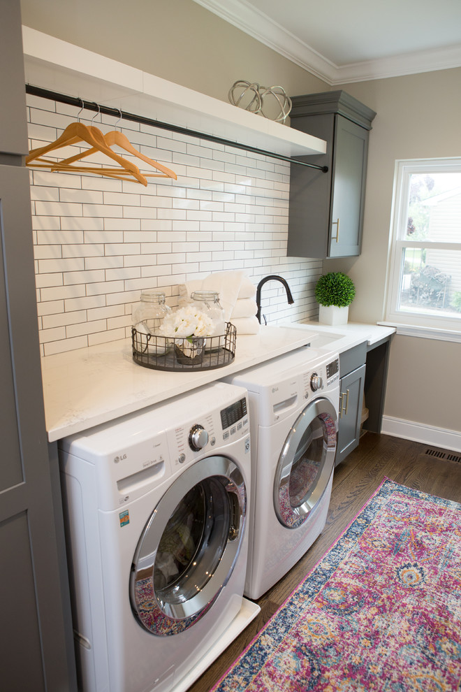 Utility room - mid-sized transitional u-shaped medium tone wood floor and brown floor utility room idea in Chicago with a farmhouse sink, shaker cabinets, quartz countertops, white backsplash, subway tile backsplash, white countertops, gray cabinets, beige walls and a side-by-side washer/dryer