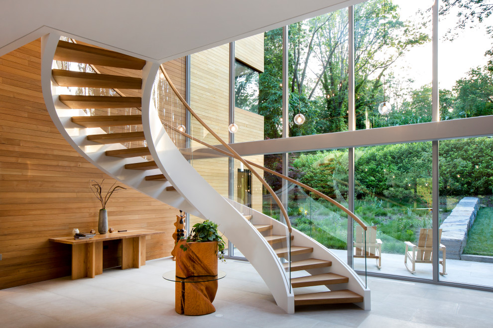 Photo of a large modern wood curved staircase in New York with open risers, metal railing and wood walls.