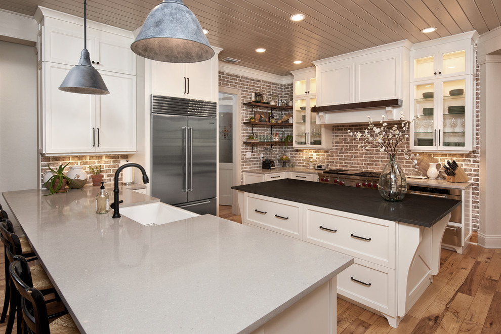 Large country kitchen in Orlando with a farmhouse sink, beaded inset cabinets, white cabinets, quartz benchtops, brown splashback, brick splashback, stainless steel appliances, medium hardwood floors, with island and brown floor.