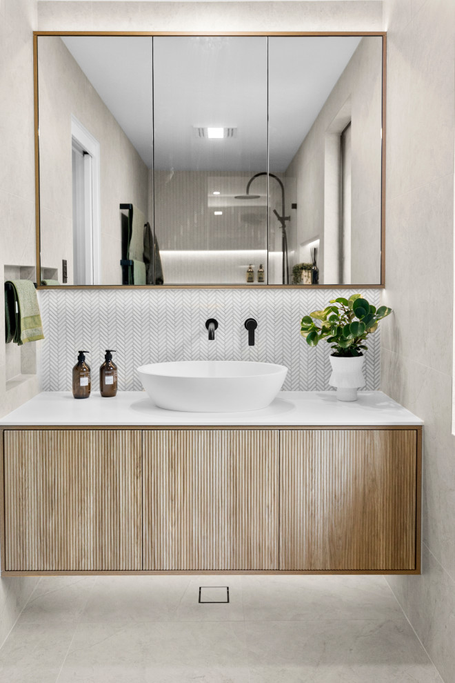 This is an example of a large contemporary 3/4 bathroom in Sydney with furniture-like cabinets, medium wood cabinets, an open shower, a one-piece toilet, multi-coloured tile, porcelain tile, multi-coloured walls, porcelain floors, a vessel sink, solid surface benchtops, multi-coloured floor, an open shower, white benchtops, a niche, a single vanity and a floating vanity.