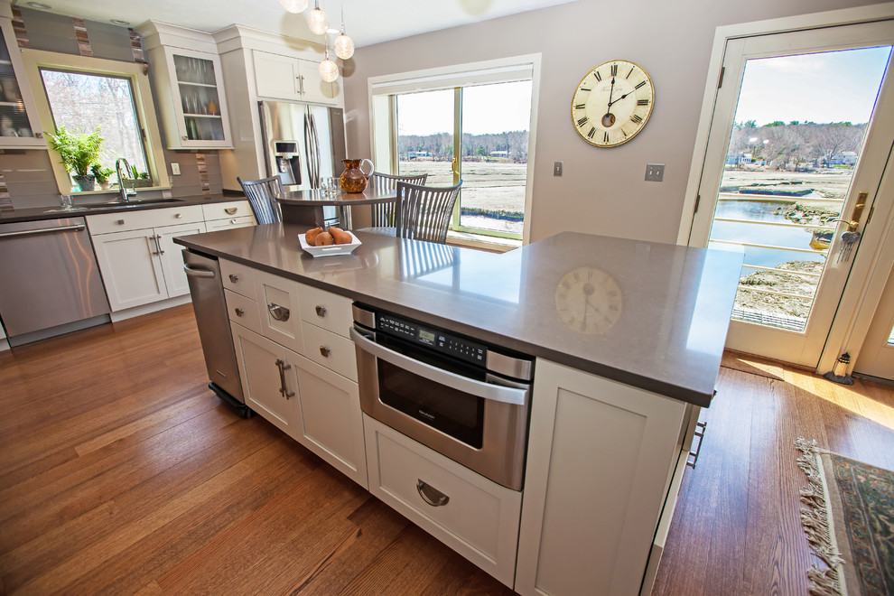 Example of a large transitional l-shaped medium tone wood floor eat-in kitchen design in Boston with an undermount sink, shaker cabinets, white cabinets, quartz countertops, gray backsplash, glass sheet backsplash, stainless steel appliances and an island