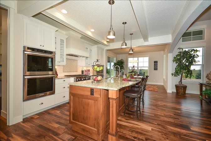 Large country single-wall open plan kitchen in Denver with a farmhouse sink, recessed-panel cabinets, white cabinets, granite benchtops, grey splashback, porcelain splashback, stainless steel appliances, medium hardwood floors and with island.
