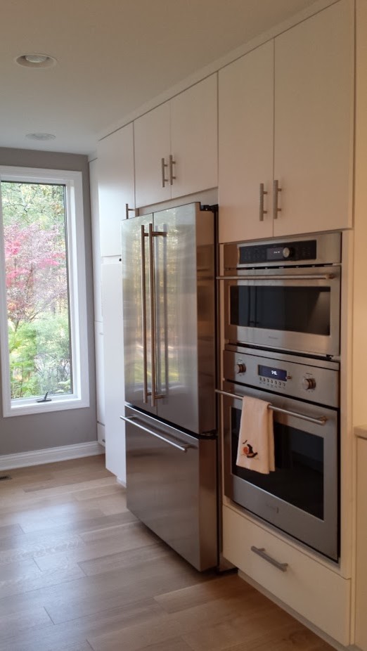 Small transitional galley medium tone wood floor enclosed kitchen photo with an undermount sink, flat-panel cabinets, white cabinets, quartz countertops, white backsplash, mosaic tile backsplash, stainless steel appliances and a peninsula