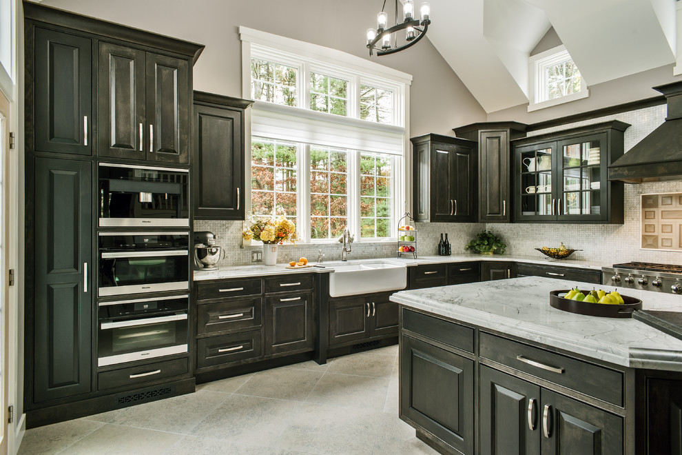 Photo of an expansive transitional l-shaped eat-in kitchen in Boston with a farmhouse sink, beaded inset cabinets, black cabinets, quartzite benchtops, grey splashback, stone tile splashback, stainless steel appliances, porcelain floors, with island and grey benchtop.