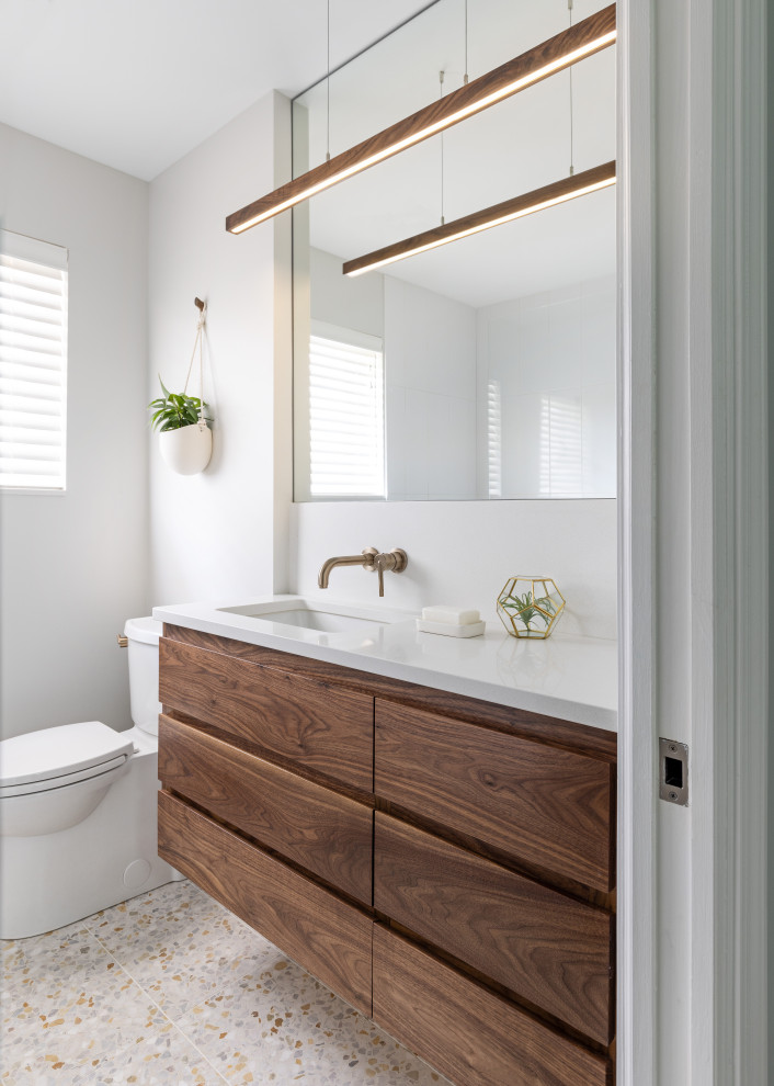 Photo of a mid-sized midcentury master bathroom in Detroit with dark wood cabinets, a single vanity, a shower/bathtub combo, white walls, terrazzo floors, beige floor, a hinged shower door, white benchtops, flat-panel cabinets, a two-piece toilet, an undermount sink, engineered quartz benchtops and a floating vanity.
