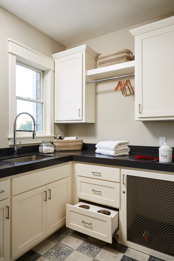 This is an example of a mid-sized traditional l-shaped dedicated laundry room in Minneapolis with an undermount sink, recessed-panel cabinets, white cabinets, quartzite benchtops, grey walls, vinyl floors, a stacked washer and dryer, multi-coloured floor and black benchtop.