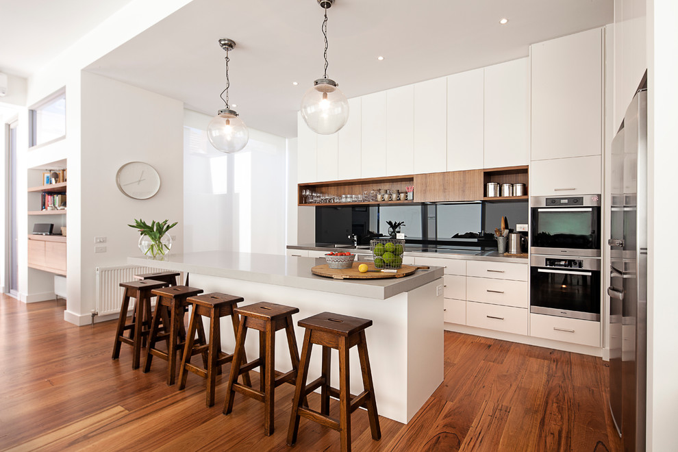 Photo of a mid-sized contemporary galley eat-in kitchen in Melbourne with an undermount sink, flat-panel cabinets, black splashback, glass sheet splashback, stainless steel appliances, medium hardwood floors and with island.