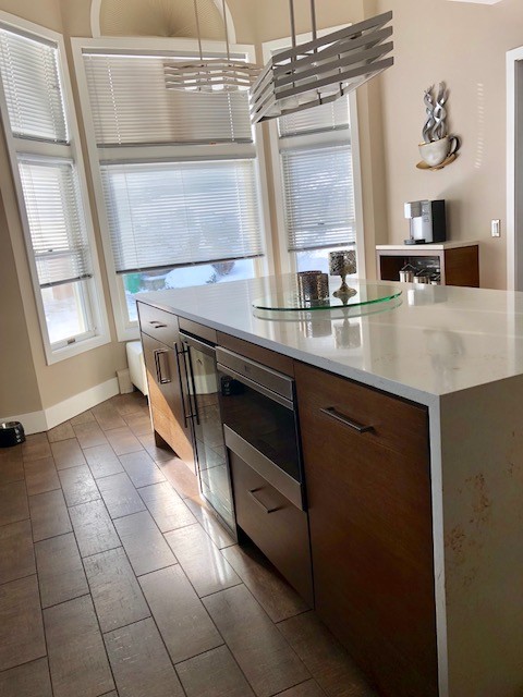 Photo of a mid-sized modern l-shaped separate kitchen in New York with an undermount sink, flat-panel cabinets, medium wood cabinets, quartz benchtops, grey splashback, matchstick tile splashback, stainless steel appliances, vinyl floors, with island, brown floor and white benchtop.