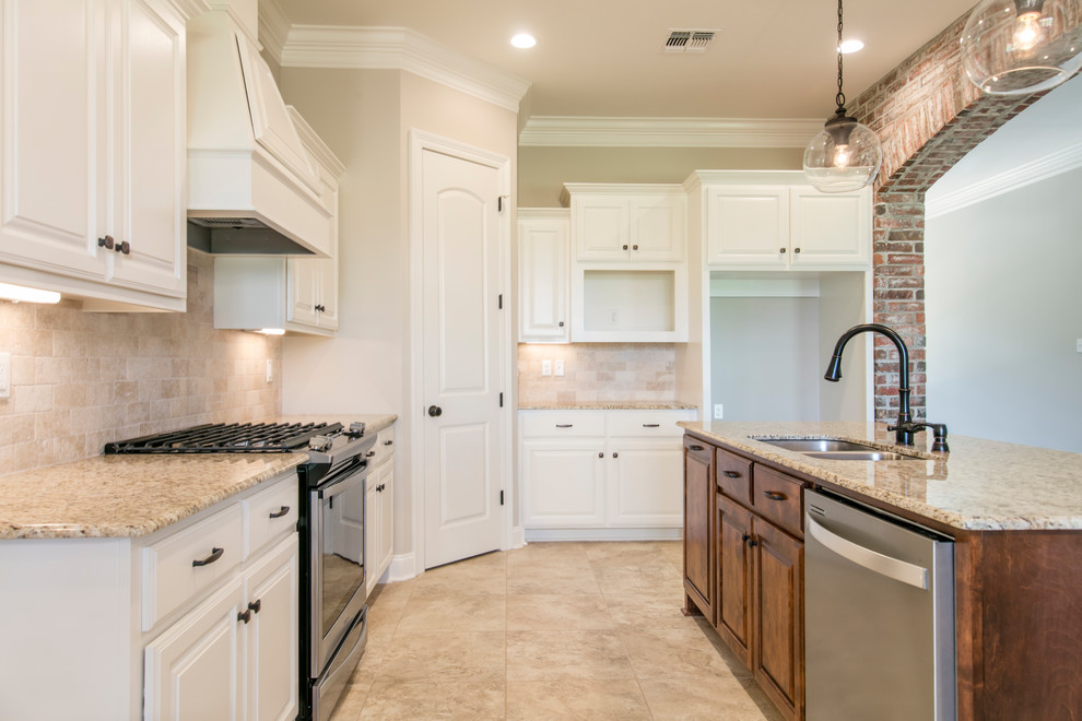 This is an example of a mid-sized traditional l-shaped eat-in kitchen in New Orleans with an undermount sink, raised-panel cabinets, white cabinets, granite benchtops, beige splashback, travertine splashback, stainless steel appliances, ceramic floors, with island, beige floor and beige benchtop.