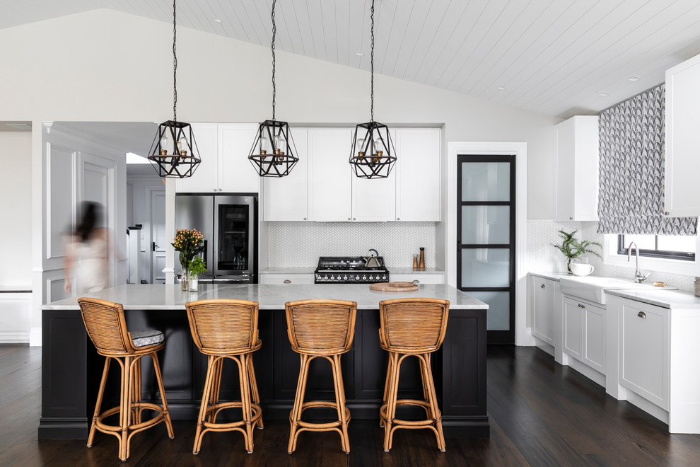 Inspiration for a transitional l-shaped kitchen in Brisbane with a farmhouse sink, shaker cabinets, white cabinets, white splashback, stainless steel appliances, dark hardwood floors, with island, brown floor and white benchtop.