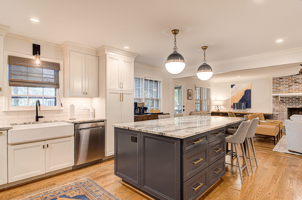 Eat-in kitchen - mid-sized transitional l-shaped medium tone wood floor and brown floor eat-in kitchen idea with a farmhouse sink, recessed-panel cabinets, white cabinets, marble countertops, white backsplash, subway tile backsplash, stainless steel appliances, an island and gray countertops