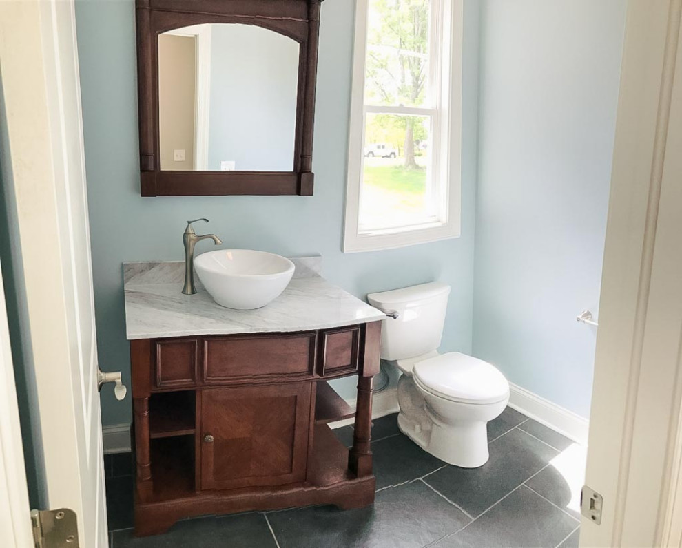This is an example of a contemporary powder room in Cleveland with shaker cabinets, medium wood cabinets, a two-piece toilet, ceramic floors, a vessel sink, marble benchtops and a freestanding vanity.