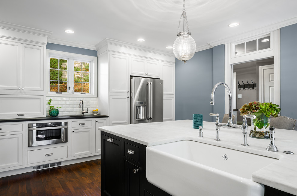 Photo of a large traditional l-shaped eat-in kitchen in Philadelphia with a farmhouse sink, recessed-panel cabinets, white cabinets, soapstone benchtops, white splashback, subway tile splashback, stainless steel appliances, dark hardwood floors and with island.