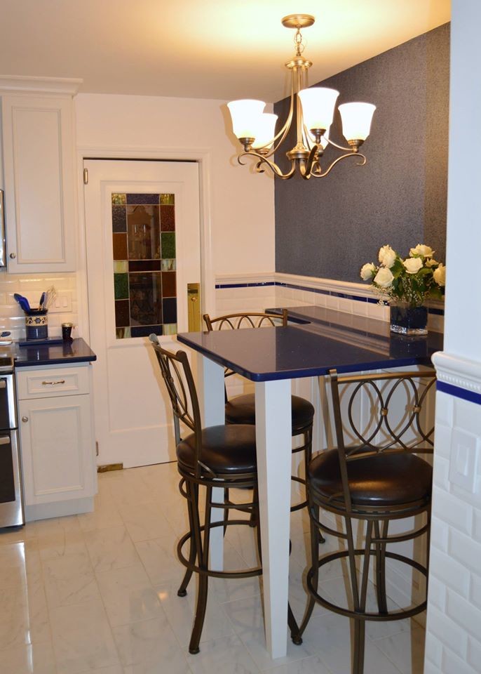Example of a large u-shaped porcelain tile eat-in kitchen design in Boston with white cabinets, white backsplash, stainless steel appliances, an island, raised-panel cabinets, quartz countertops and ceramic backsplash