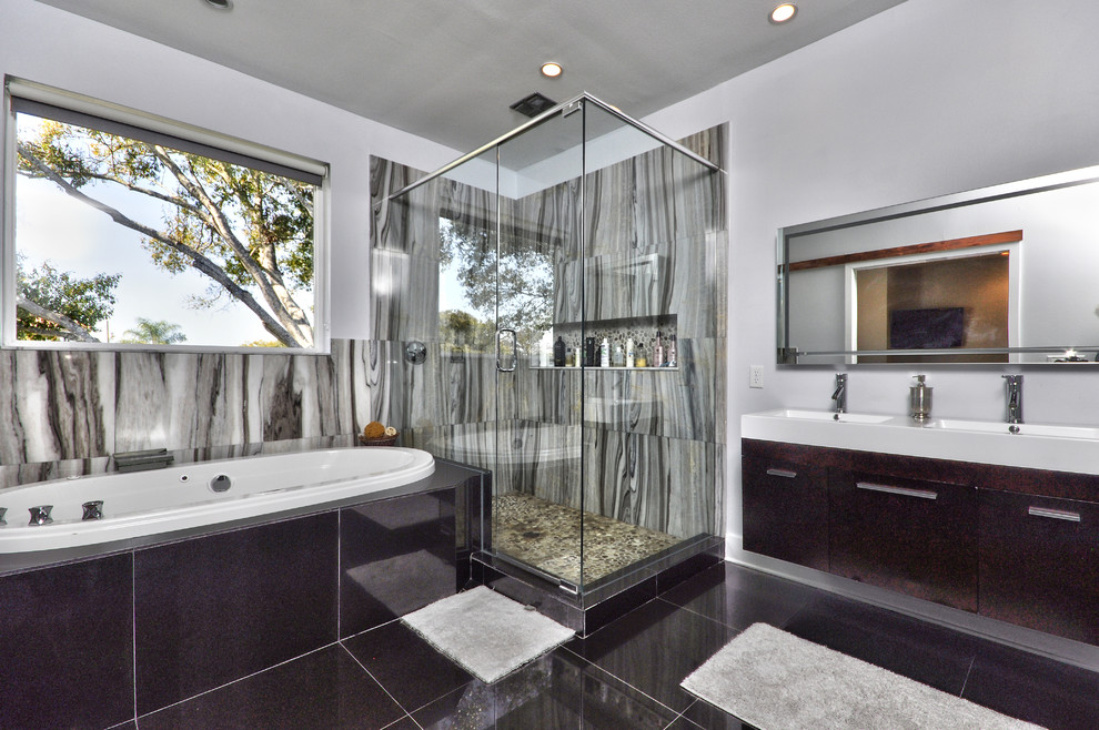 Photo of a large modern master bathroom in Tampa with flat-panel cabinets, dark wood cabinets, a drop-in tub, a corner shower, a two-piece toilet, black and white tile, cement tile, white walls, ceramic floors, an integrated sink and limestone benchtops.