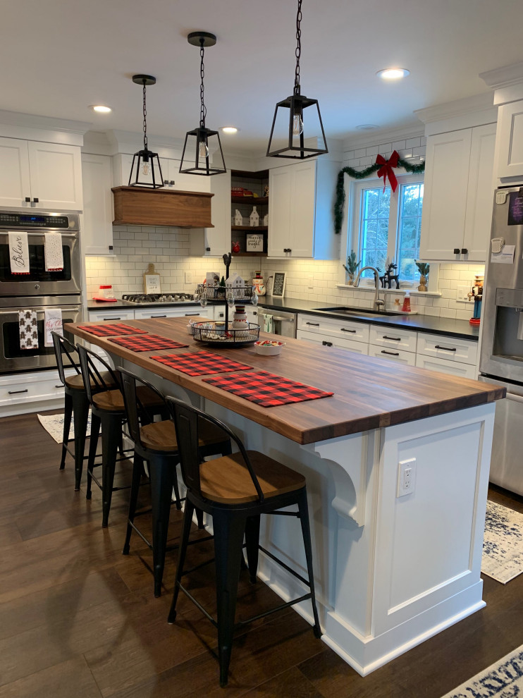 Inspiration for a large transitional l-shaped dark wood floor and brown floor eat-in kitchen remodel with a single-bowl sink, flat-panel cabinets, white cabinets, quartz countertops, white backsplash, subway tile backsplash, stainless steel appliances, an island and black countertops