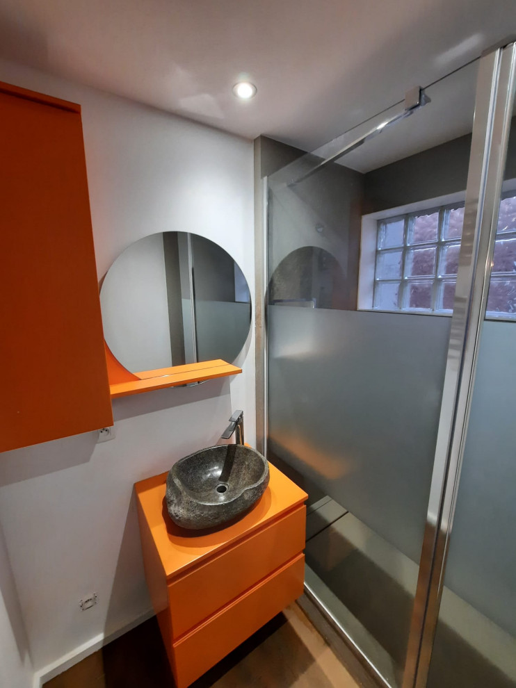 Modelo de cuarto de baño principal, único y flotante actual pequeño con puertas de armario naranjas, ducha a ras de suelo, suelo vinílico y suelo multicolor