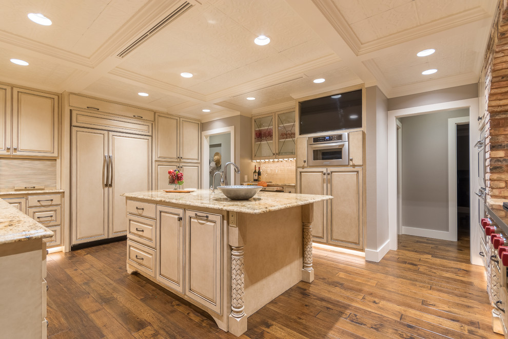 Large transitional u-shaped medium tone wood floor enclosed kitchen photo in Austin with a double-bowl sink, raised-panel cabinets, white cabinets, granite countertops, beige backsplash, stone tile backsplash, paneled appliances and an island