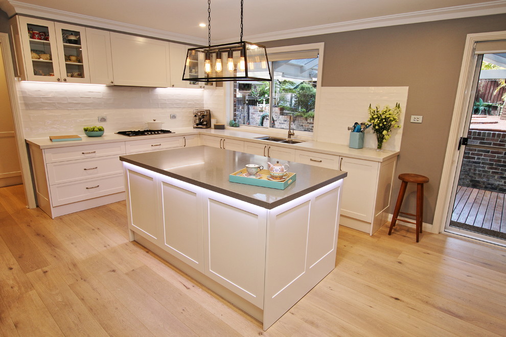Large eclectic l-shaped kitchen pantry in Sydney with an undermount sink, shaker cabinets, white cabinets, quartz benchtops, white splashback, subway tile splashback, stainless steel appliances, light hardwood floors, with island and brown floor.