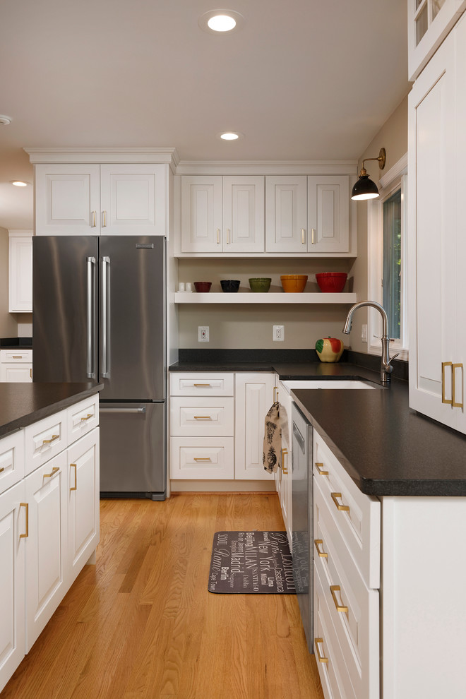 Enclosed kitchen - mid-sized transitional galley light wood floor enclosed kitchen idea in DC Metro with a farmhouse sink, raised-panel cabinets, white cabinets, solid surface countertops, gray backsplash, ceramic backsplash, stainless steel appliances and an island