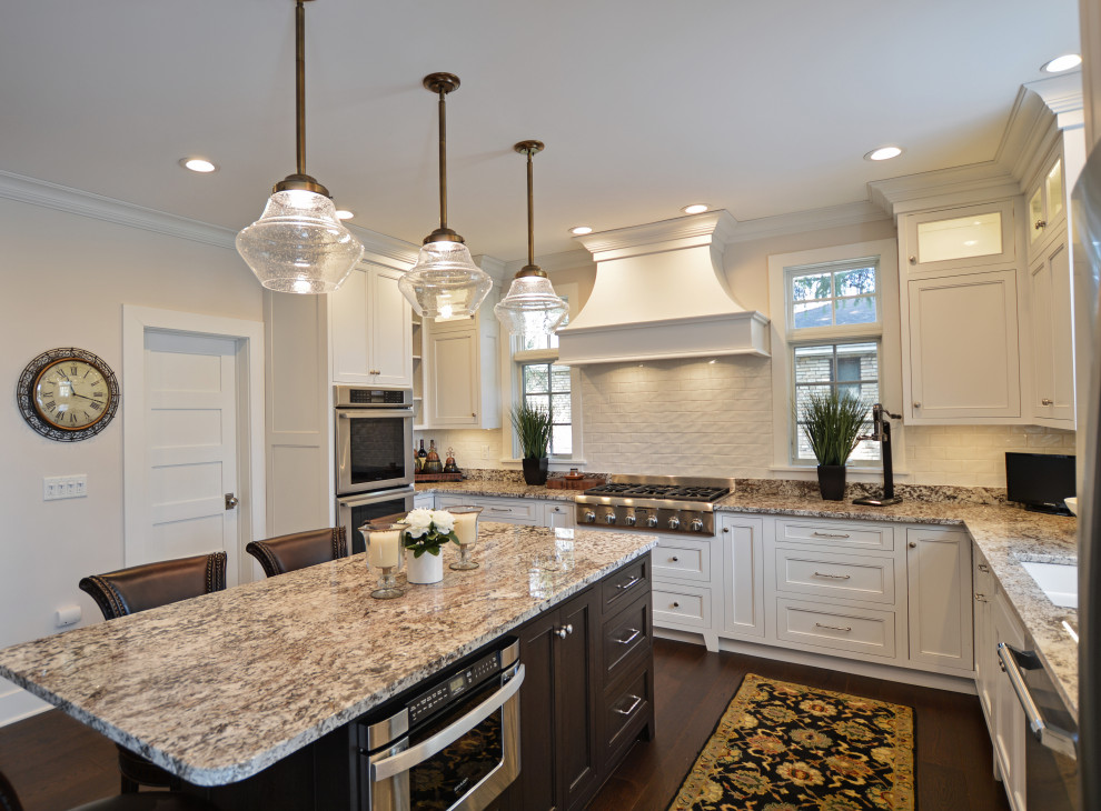 Eat-in kitchen - transitional dark wood floor and brown floor eat-in kitchen idea with an undermount sink, shaker cabinets, white cabinets, granite countertops, white backsplash, ceramic backsplash, stainless steel appliances, an island and beige countertops